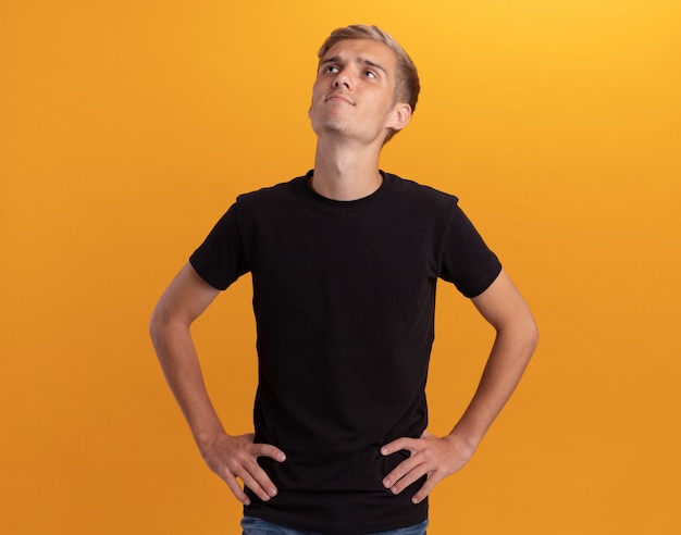 Free photo impressed looking up young handsome guy wearing black shirt putting hands on hip isolated on yellow wall