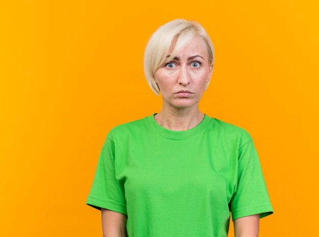 Impressed middle-aged blonde slavic woman looking at camera isolated on yellow background with copy space