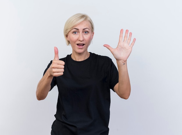 Impressed middle-aged blonde slavic woman looking at camera showing six with hands isolated on white background with copy space