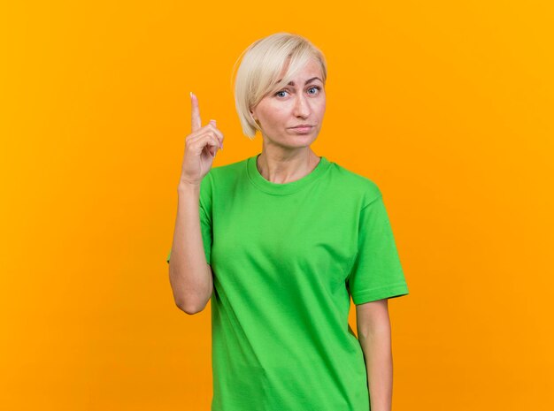 Impressed middle-aged blonde slavic woman looking at front pointing up isolated on yellow wall with copy space