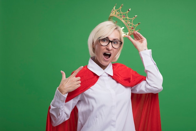 自分自身を指している頭の上に王冠を保持している眼鏡をかけている赤いマントの印象的な中年の金髪のスーパーヒーローの女性
