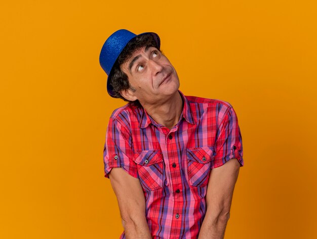 Impressed middle-aged caucasian party man wearing party hat looking up isolated on orange background with copy space