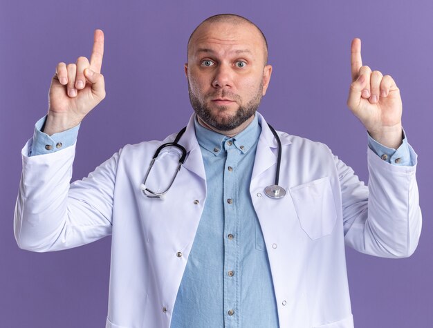 Impressed middle-aged male doctor wearing medical robe and stethoscope pointing up 