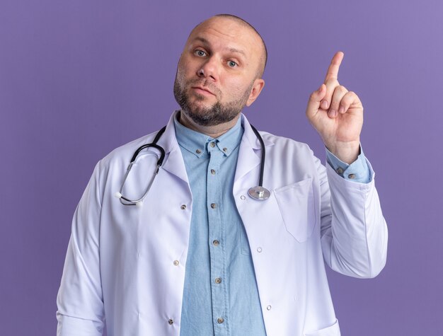 Impressed middle-aged male doctor wearing medical robe and stethoscope pointing up 