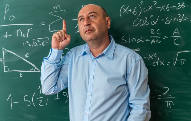 impressed middle-aged male teacher standing in front blackboard points at up