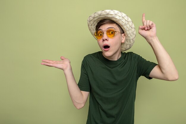 Impressed points at up young handsome guy wearing hat with glasses 