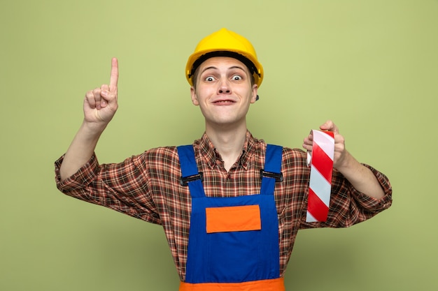 Foto gratuita punti impressionati su un giovane costruttore maschio che indossa un'uniforme che tiene del nastro adesivo