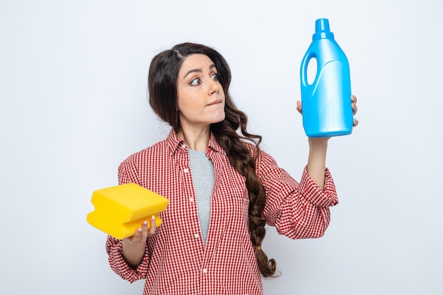 Impressed pretty caucasian cleaner woman holding and looking at toilet cleaner and keeping sponge 