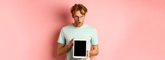 Free photo impressed redhead man in glasses showing blank digital tablet screen and looking in awe at display s