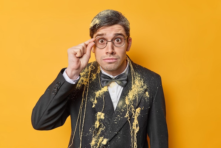 Free Photo impressed shocked man dressed in formal festive suit keeps hand on rim of spectacles smeared with serpantine spray reacts on surprising news isolated over yellow background celebrates something