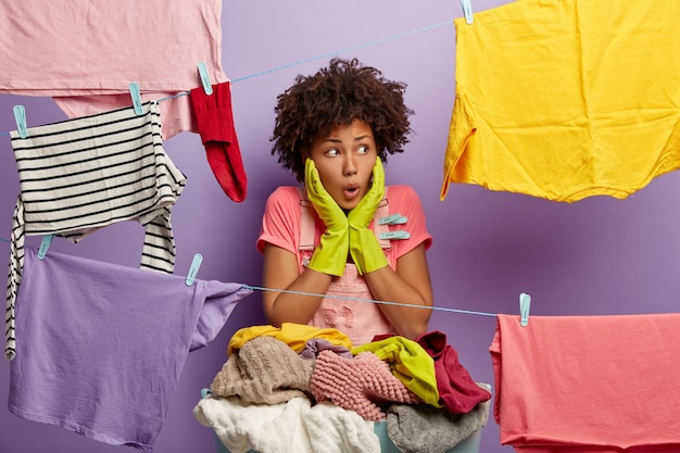 Free photo impressed shocked young woman with an afro posing with laundry in overalls