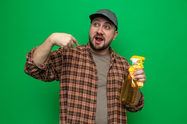 Impressed slavic cleaner man holding cleaning cloths and spray cleaner pointing at himself