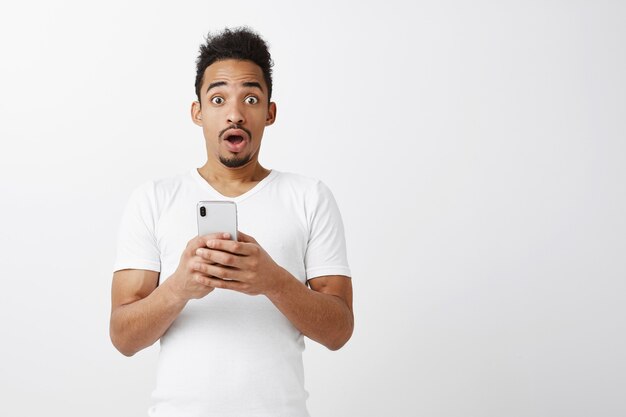 Impressed and surprised handsome african american guy using mobile phone, gasping astonished