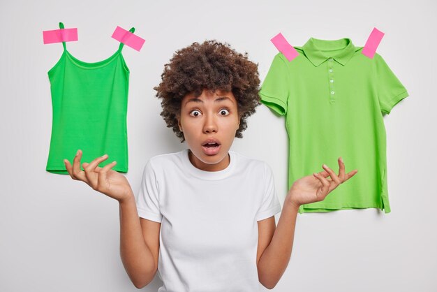 Impressed woman spreads palms looks indignant keeps widely opened eyes and mouth being embarrassed poses against white background with green casual t shirts plastered behind Omg what to do