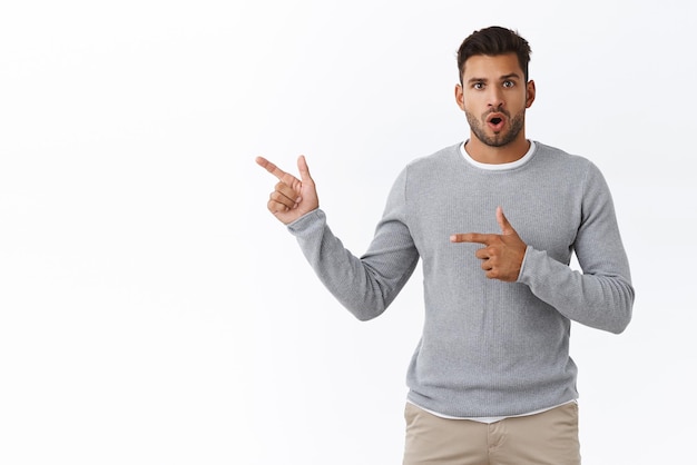 Impressed and wondered goodlooking caucasian male model in modern grey sweater gasping amused say wow fascinated pointing left curious found interesting product and gather info about it