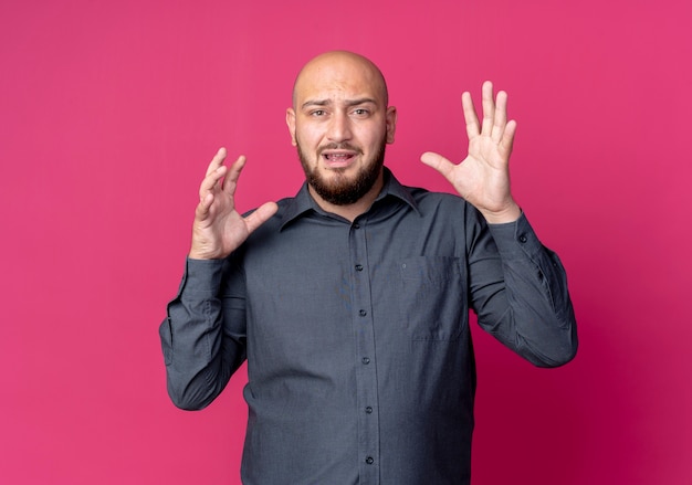 Impressed young bald call center man keeping hands in air isolated on crimson  with copy space