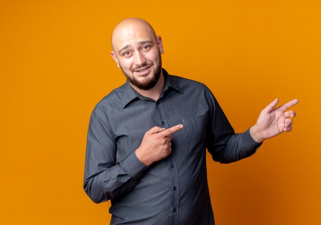 Impressed young bald call center man pointing at side isolated on orange  with copy space