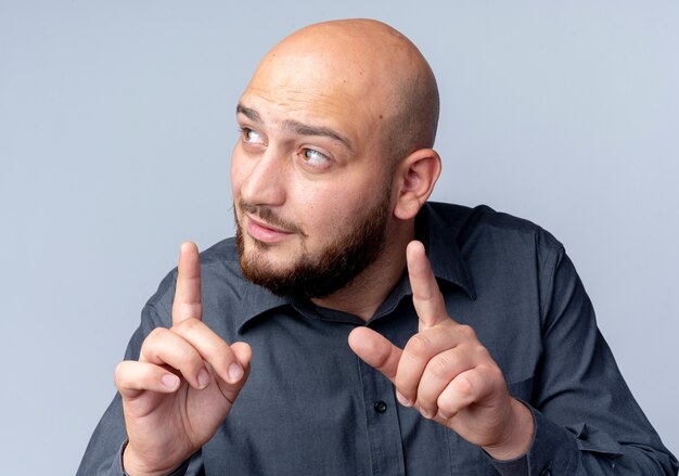 Impressed young bald call center man raising fingers looking at side isolated on white 