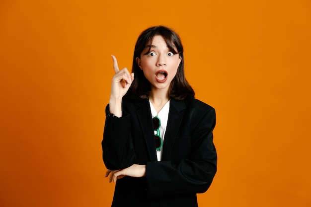 Impressed young beautiful female wearing black jacket isolated on orange background