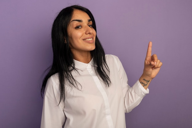 Free photo impressed young beautiful girl wearing white t-shirt points at up isolated on purple