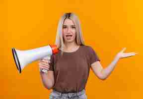 Free photo impressed young blonde girl holding speaker showing empty hand on isolated orange space