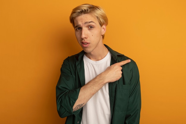 Impressed young blonde guy wearing green t-shirt points at side