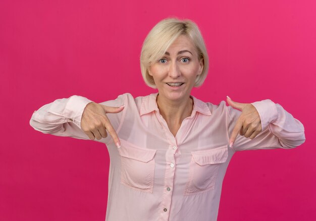 Impressed young blonde slavic woman pointing down isolated on pink background