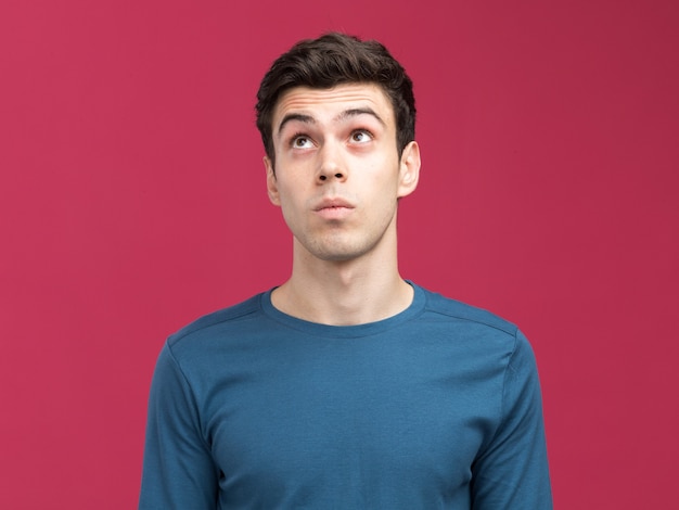 Impressed young brunette caucasian man looking up isolated on pink wall with copy space