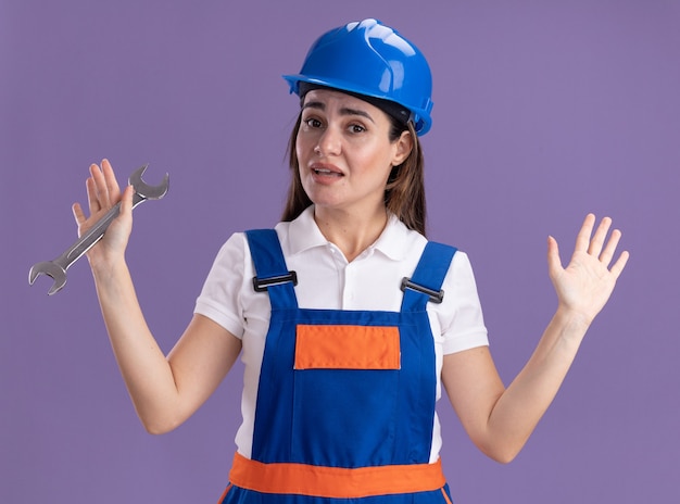 보라색 벽에 고립 된 손을 확산 오픈 엔드 렌치를 들고 유니폼에 감동 된 젊은 작성기 여자