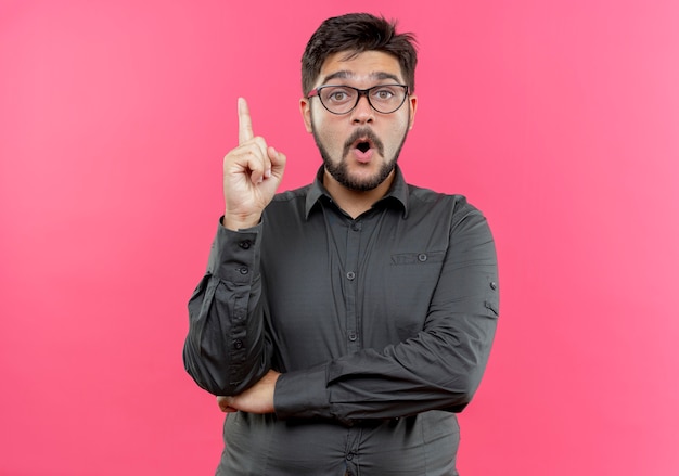 Free photo impressed young businessman wearing glasses points at up isolated on pink wall