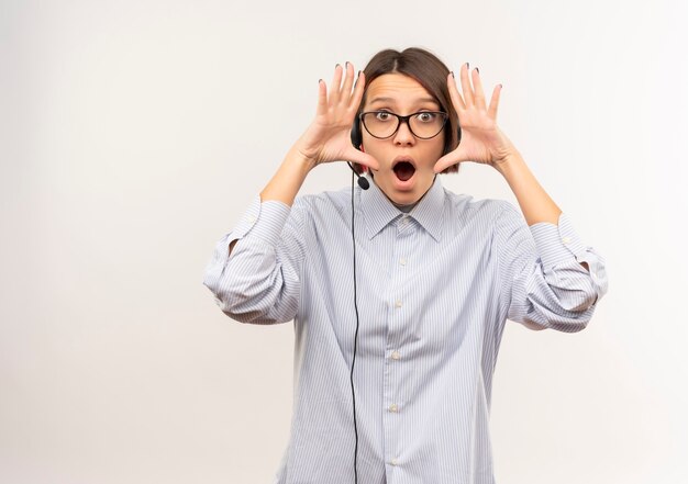 Impressed young call center girl wearing glasses and headset keeping hands near face isolated on white  with copy space