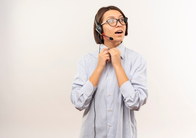 Impressed young call center girl wearing glasses and headset looking at side keeping hands together isolated on white  with copy space