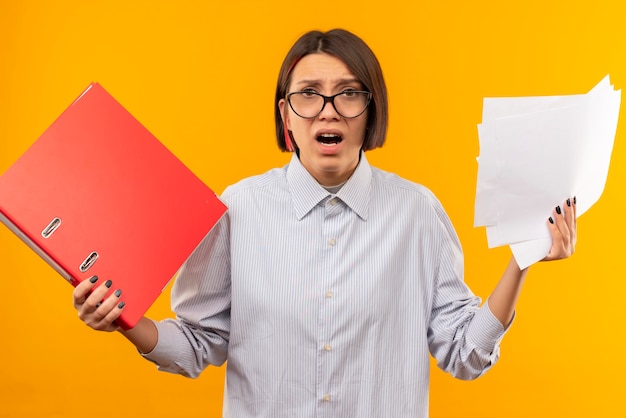 Impressed young call center girl wearing glasses holding folder and documents isolated on orange 