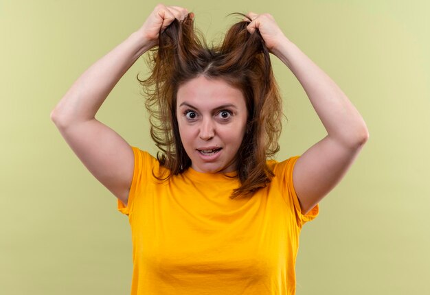 Impressed young casual woman holding her hair on isolated green space