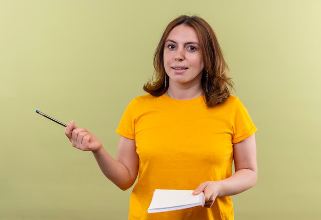 Impressed young casual woman holding pen and note pad on isolated green space