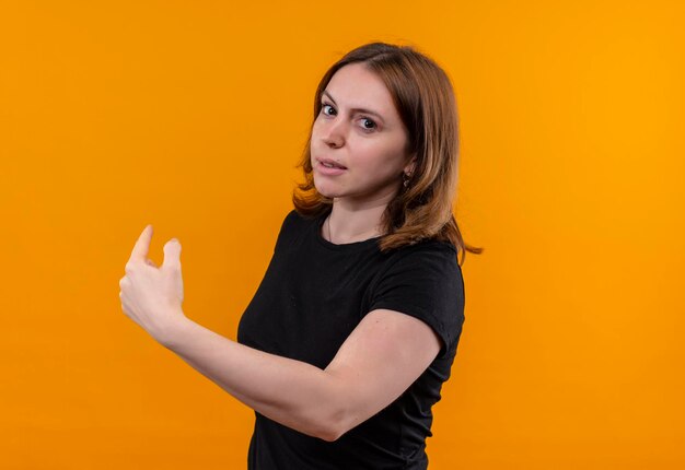 Impressed young casual woman pointing behind on isolated orange space with copy space