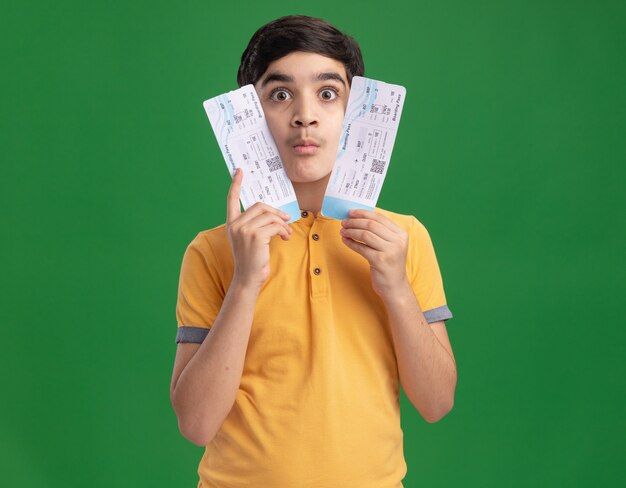 Впечатленный молодой кавказский мальчик, держащий билеты на самолет, касаясь ими лица