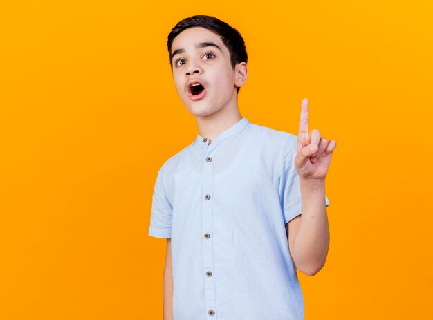 Impressed young caucasian boy looking at camera raising finger isolated on orange background with copy space