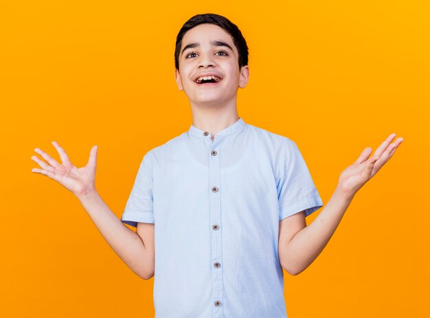 Impressed young caucasian boy looking at camera showing empty hands isolated on orange background