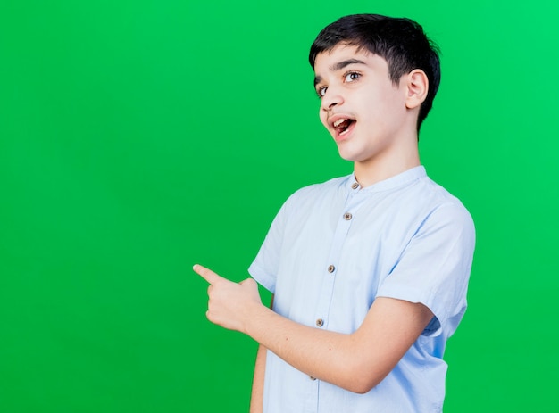 Impressed young caucasian boy  pointing behind isolated on green wall with copy space