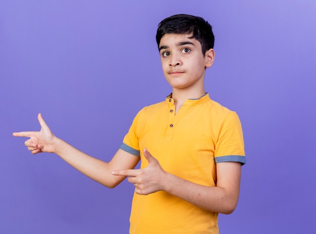 コピースペースで紫色の壁に隔離された側を指している印象的な若い白人の少年