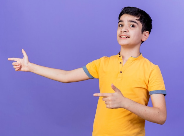 紫色の壁に隔離された側を指している印象的な若い白人の少年
