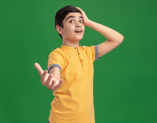 Free photo impressed young caucasian boy putting hand on head stretching hand out