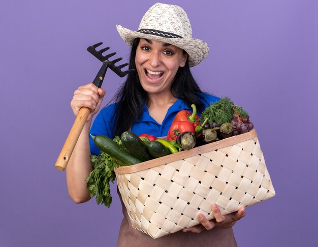野菜と熊手のバスケットを保持している制服と帽子を身に着けている印象的な若い白人の庭師の女性