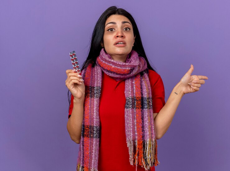 मुफ़्त फोटो impressed young caucasian ill girl wearing scarf holding pack of capsules looking at camera pointing at side isolated on purple background with copy space