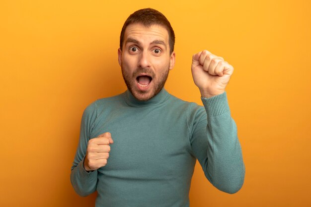 Impressed young caucasian man clenching fists looking at camera isolated on orange background