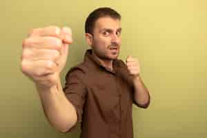 Free photo impressed young caucasian man looking at camera doing boxing gesture isolated on olive green background with copy space