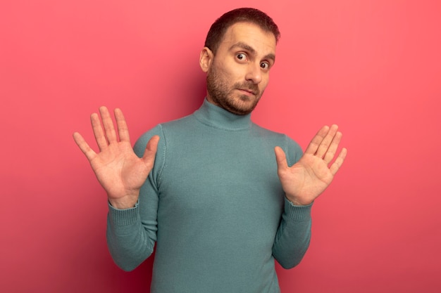 Impressed young caucasian man  showing empty hands isolated on crimson wall