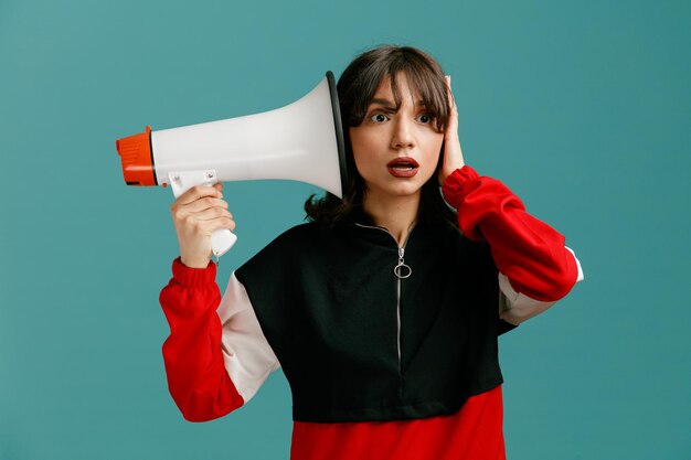 Impressed young caucasian woman looking at side pointing speaker at her ear closing another ear with hand isolated on blue background