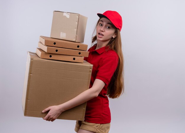 Impressed young delivery girl in red uniform holding packages and boxes on isolated white space with copy space